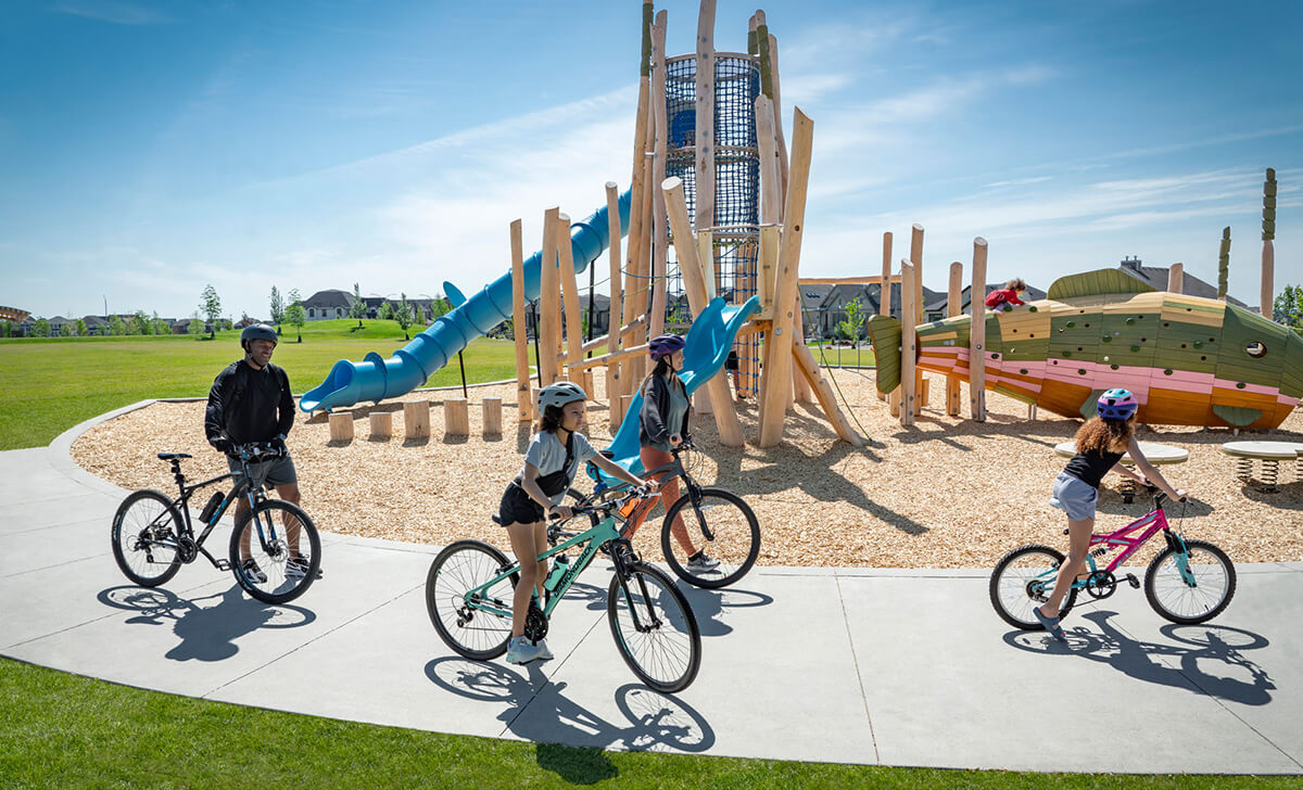 Family of 4 riding bicycles around playground